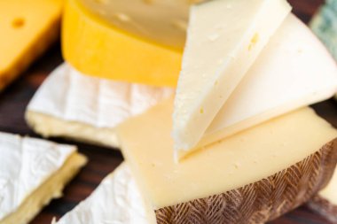 Koyu ahşap arka planda büyük gurme peynir dilimleri var..