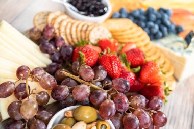 Aperatif olarak sunulan tahtanın üzerinde gurme peyniri, kraker ve meyve var..