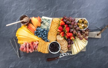 Düz yatıyordu. Aperatif olarak sunulan tahtanın üzerinde gurme peyniri, kraker ve meyve var..