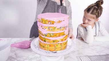 Adım adım. Pembe tereyağlı krema kaplı yuvarlak funfetti kek katmanları.