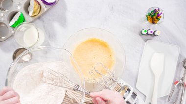 Düz yatıyordu. Adım adım. Vanilyalı Mardi Gras kekleri pişirmek için karışımı elektrikli mikserle karıştırıyorum..