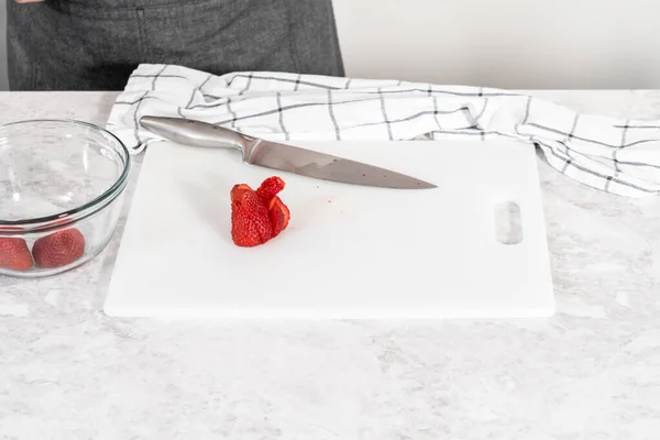 イチゴのバタークリームの霜降りを準備するために白いまな板に新鮮なイチゴをカット — ストック写真