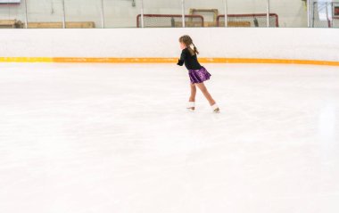 Küçük kız buz pateni pistinde artistik patinaj yapıyor..