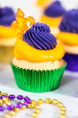 Mardi Gras vanilyalı kekler folyo kaplarda ve İtalyan tereyağlı kremayla süslenmiş..