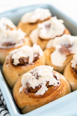 Taze pişmiş tarçınlı rulo, beyaz kremalı, mavi bir tavada..