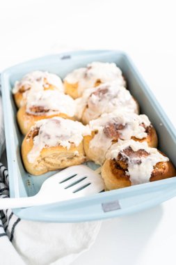 Taze pişmiş tarçınlı rulo, beyaz kremalı, mavi bir tavada..