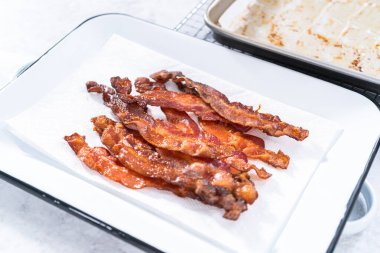 Beyaz tepside pişmiş pastırma şeritleri ve kağıt havlu..