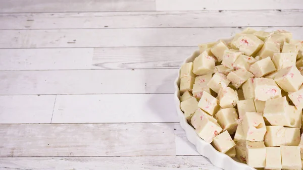 Step by step. Candy cane fudge cut in small cubes on a white serving dish.