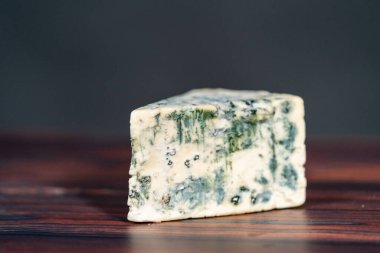 Koyu ahşap arka planda büyük bir dilim mavi peynir..