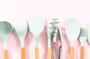 Pembe arka planda ahşap saplı yeni mavi silikon mutfak aletleri..