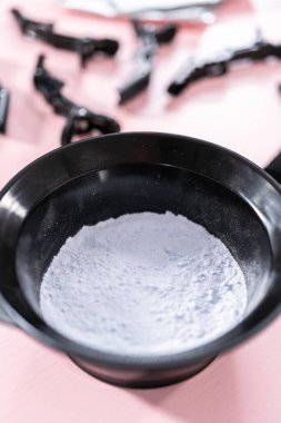 Siyah plastik bir kasede pembe arka planda saç boyası tozu..