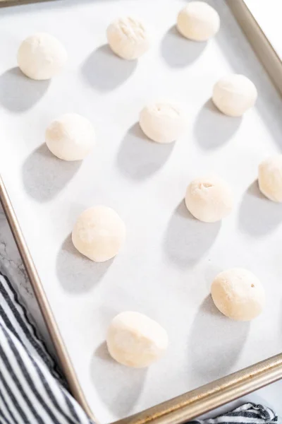 Rising frozen dinner rolls on a baking sheet lined with parchment paper.
