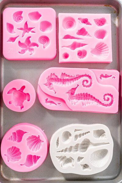 Filling silicone chocolate molds in the shape of mermaid tails and seashells with melted chocolate.