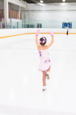 Güzel pembe elbiseli, çiçekli küçük bir kız buz pateni pistinde artistik patinaj yapıyor..