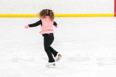 Küçük kız buz pistinde artistik patinaj yapıyor..