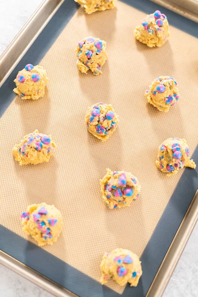 Chilled cookie dough scoops on the baking sheet to bake unicorn chocolate chip cookies.