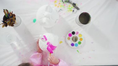 Küçük kız Cadılar Bayramı balkabağını akrilik boyayla boyuyor.