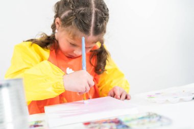 Evde akrilik boyalı bir sanat projesi üzerinde çalışan küçük bir kız..