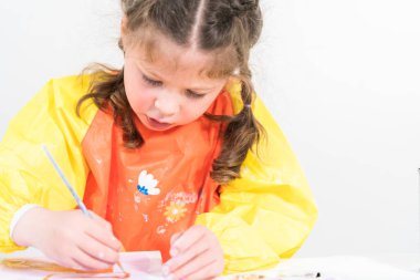 Evde akrilik boyalı bir sanat projesi üzerinde çalışan küçük bir kız..