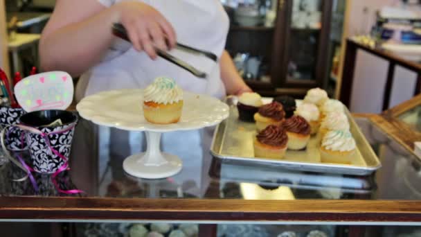 Пекарь в кондитерской выкладывает кексы — стоковое видео