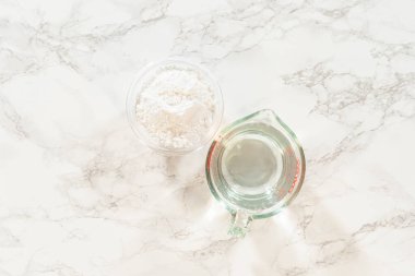 Pudra şekeriyle dolu bir cam kase ve mermer bir yüzeyde suyla ölçme kabı. Paskalya Kurabiyesi Sandviçi için ahududu kremalı malzeme hazırlamak için mükemmel..