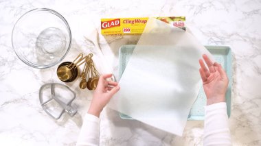 Parker, Colorado, ABD-6 Mayıs 2025 - Bir kişi bir parşömen kağıdını pastel mavi fırın tepsisine yerleştirir, etrafını kaseler ve mermer tezgahın üzerindeki pişirme aletleri sarar. Kompozisyona göre...