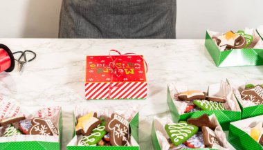 Orta menzilli bir fotoğraf, düzgünce düzenlenmiş Noel kurabiyesi hediye kutularıyla dolu bir şenlik masası yakalıyor. Sahnede kırmızı ve beyaz tatil temalı kutular ve kırmızı ile bağlanmış zarif beyaz kutular yer alıyor.