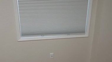 Bir kişi uzanıyor ve iyi aydınlatılmış bir iç mekanda pencerenin üzerindeki beyaz kabloyu nazikçe çekiyor. Odak noktası, temiz bir odadaki körlerin hareketleri ve hareketleridir..