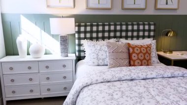 Yeşil ve beyaz renkli çarpıcı geometrik bir yatak başlığı olan rahat yatak odası, klasik düğmeleri olan beyaz bir şifonyer, parlak bir pencereye dayanıyor..