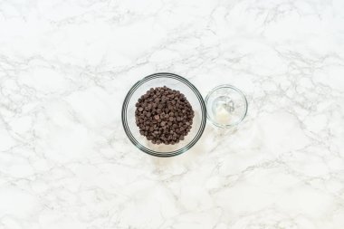 Preparing ingredients for the chocolate dip for peppermint sugar cookies, including a glass bowl of dark chocolate chips and a small bowl of crushed peppermint. Captured from an overhead view on a
