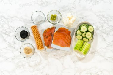 Krem peynir, füme somon dilimleri, kabak kurdeleleri, soya sosu, susam tohumu ve boru torbası da dahil olmak üzere tütsülenmiş somon peynirli peynirli rulo hazırlamak için gereken malzemeler..