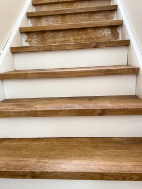 View from the top of a staircase looking down on clean wooden steps and white risers. The lighting highlights the grain of the wood and contrast with the white.