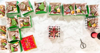 Noel kurabiyesinin hediye kutusunu saran, güzelce hazırlanmış Noel kutuları ile çevrili, tepeden tırnağa bir el resmi. Sahnede zencefilli kurabiye, şenlikli ambalajlar ve