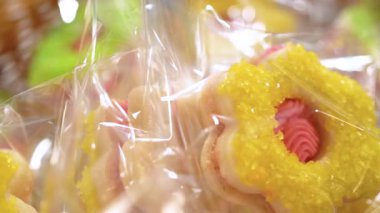 Detaylı bir çekimde plastik desen, şeker kristalleri ve pastel renklerin vurgulandığı pembe ve sarı çiçekli kurabiyeler ortaya çıkmaktadır. Fırın ürünleri promosyonları, tatlı makaraları için ideal.