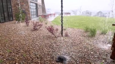 Yağmur suyu, fırtına sırasında dikey bir zincire bağlı arka bahçedeki çakıl kanalına akar. Bölge ıslak ve nehir taşlarıyla kaplı..