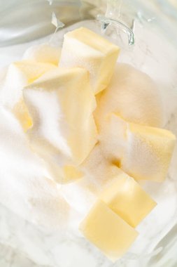 Karıştırma kabında şeker ve tereyağı küplerinin üst görüntüsü, Klasik Şekerli Kurabiye Hamuru 'nun ilk adımı olarak kremaya hazır. Malzemeler karıştırma için konumlandırılmış, bir anahtar adım