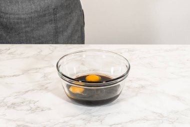 Cam bir kasede iki yumurta ve koyu pekmezin yan görüntüsü. Lezzetli Turuncu Zencefilli Kurabiye Kurabiyesi 'nin ıslak malzemelerini oluşturuyor. Koyu pekmez hamura zengin rengini ve lezzetini verir..