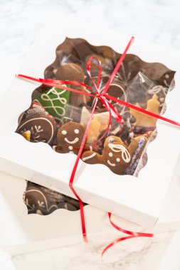 Yakın plan bir perspektiften çekilen beyaz tatil kurabiye kutularının zarif kesme pencereleri içerisindeki süslü Noel kurabiyelerini ortaya çıkarıyor. Kırmızı kurdele şenlikli bir dokunuş ekliyor.