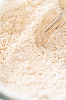 Klasik Zencefilli Kurabiye Kurabiyesi Hamuru 'nu hazırlarken atılan ilk adımların bir parçası olan un cam bir kasede çırpılırken yakın plan görüntüsü. Çırpma, bileşenleri birleştirmeden önce kuru malzemeyi eşit olarak karıştırmaya yardımcı olur