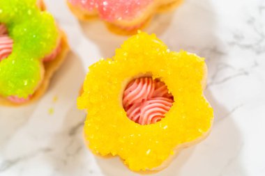 A yellow sugar-coated Easter Cookie Sandwich with Raspberry Buttercream sits on a marble background, showcasing the creamy center.