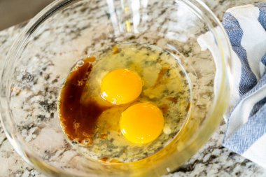 İki çiğ yumurta ve granit mutfak tezgahında karıştırma kabının içindeki vanilya özü. Yakınlarda mavi bir havlu var..