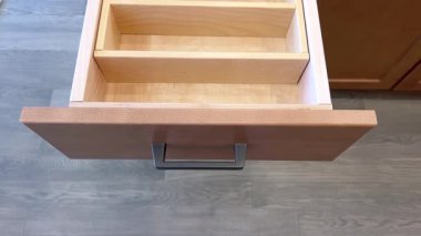 Ahşap bir mutfak çekmecesini ayırıcılarla açan bir elin yakın çekim videosu. Modern mutfak ortamında hafif aydınlatma.