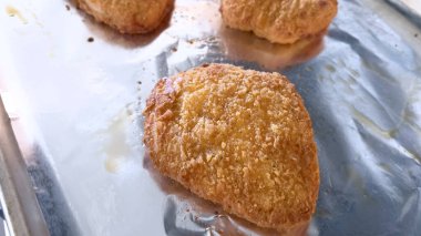 Folyo kaplı tepside pişen altın sarısı ekmekli tavuk köftelerinin yakın çekim görüntüsü. Yemekler çıtır çıtır ve ev ortamında pişmiş görünüyor..