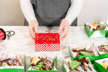 Orta menzilli bir fotoğraf, düzgünce düzenlenmiş Noel kurabiyesi hediye kutularıyla dolu bir şenlik masası yakalıyor. Sahnede kırmızı ve beyaz tatil temalı kutular ve kırmızı ile bağlanmış zarif beyaz kutular yer alıyor.
