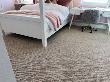 Beyaz yataklı, pembe battaniyeli, desenli tarafsız halılı modern kızların yatak odası. Beyaz bir masa ve sahte kürk sandalye boşluğu doldurur..