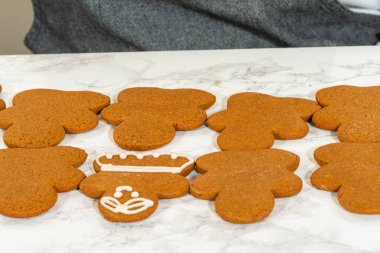 A group of gingerbread girl cookies partially decorated with royal icing, displayed alongside undecorated cookies.
