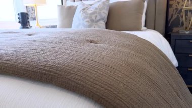 Dökümlü çarşafları ve kumaş kıvrımlarını gösteren bir yatağın ayağının detaylı görüntüsü. Yumuşak, dağınık doğal ışık sıcacık havaya katar..