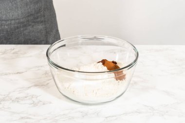 Amber zencefilli kurabiye hamuru için un ve baharat içeren bir karıştırma kabının yan görüntüsü, mermer tezgahın üzerine yerleştirilmiş, arka planda bir kişi,