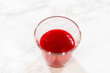 Parlak kırmızı ahududu püresi mermer bir yüzey üzerinde açık bir bardakta, ahududu kremalı Paskalya Kurabiyesi Sandviçi 'nde kullanılmaya hazır..