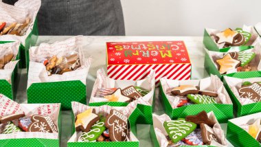 Orta menzilli çekimler bir dizi Noel kurabiyesi hediye kutularını düzgünce bir masanın üzerinde sergiliyor. Her yeşil kutu süslü zencefilli kurabiyelerle dolu, eldivenler de dahil.